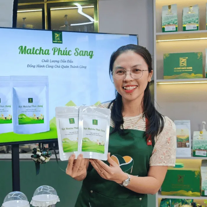 Giảng viên Ly Phạm cầm hai gói bột matcha Phúc Sang tại gian trưng bày nguyên liệu